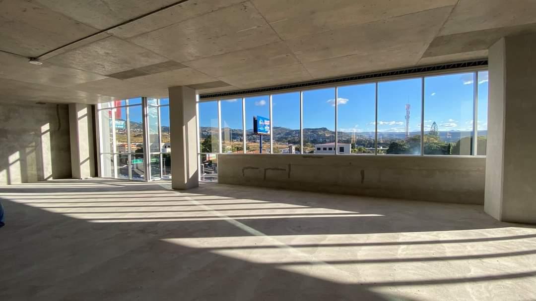 Planta de oficina en obra gris con ventanales de piso a techo y vista a las montañas de Tegucigalpa