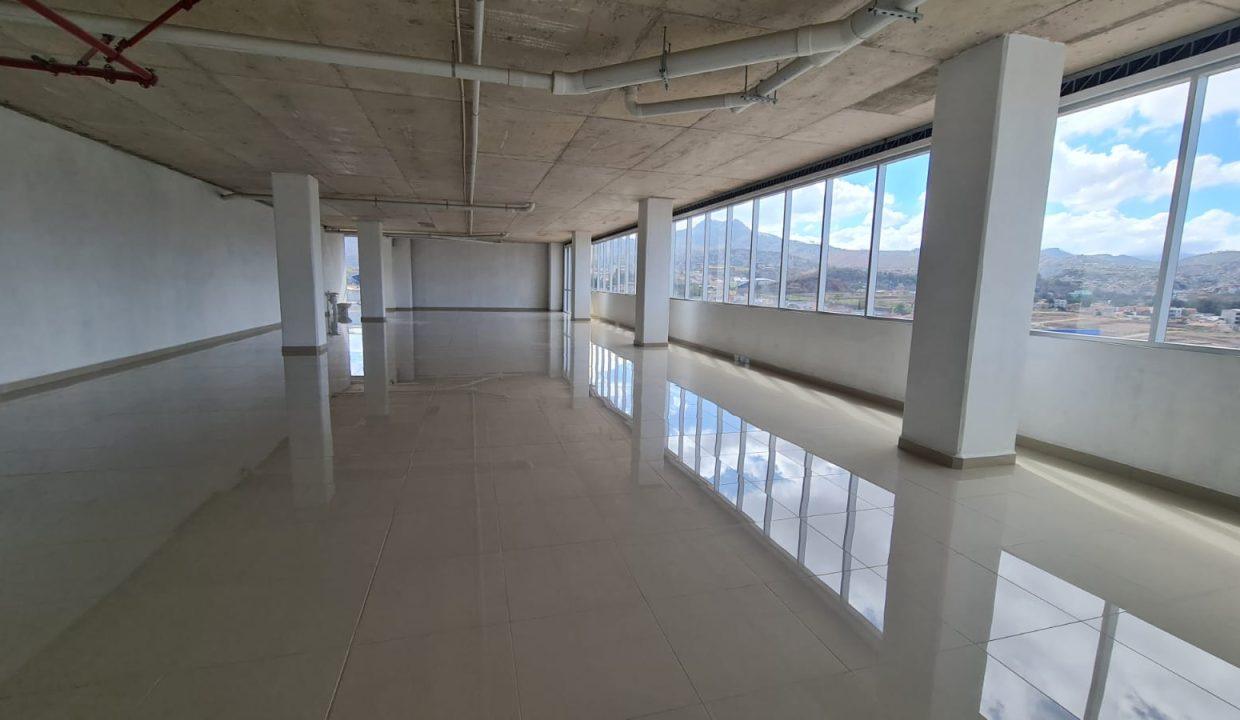 Planta de oficina en obra gris con piso cerámico, columnas estructurales y ventanales
